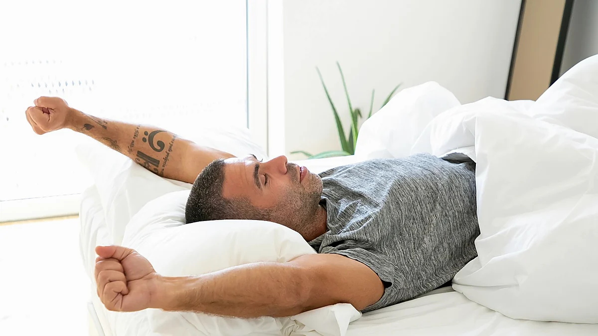 Man stretching after waking in a softly lit bedroom